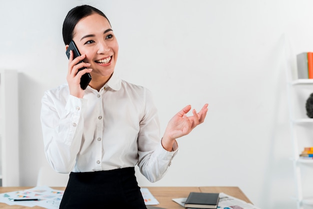 Retrato de una empresaria joven sonriente que habla en el teléfono móvil en la oficina