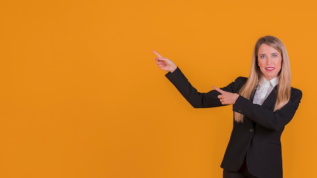 Retrato de una empresaria joven sonriente que presenta algo contra un fondo naranja