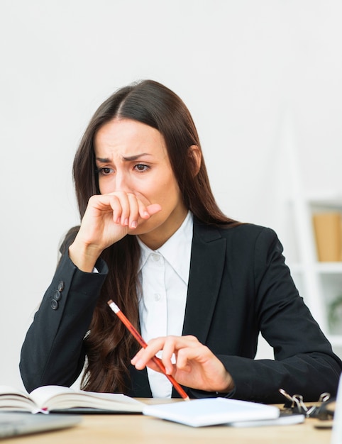 Retrato de la empresaria joven triste que sostiene el lápiz rojo en su mano que llora