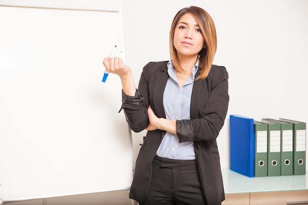 Retrato de una empresaria seria sosteniendo un marcador junto a una pizarra, lista para comenzar su presentación