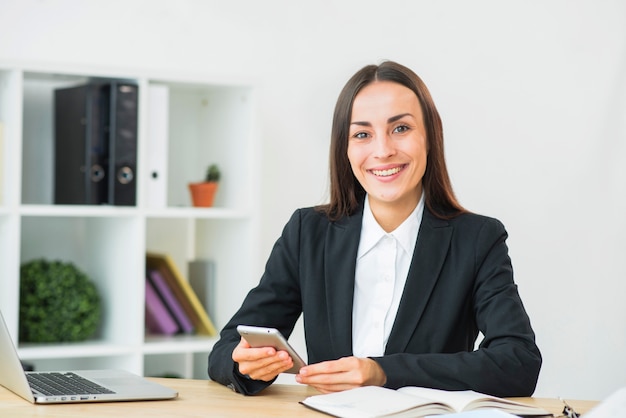 Retrato de una empresaria sonriente joven que sostiene smartphone disponible