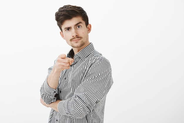 Retrato de empresario masculino alegre confiado con bigote, señalando y levantando la ceja, invitando a la persona a ir a la barra juntos, aprobando un buen punto de vista