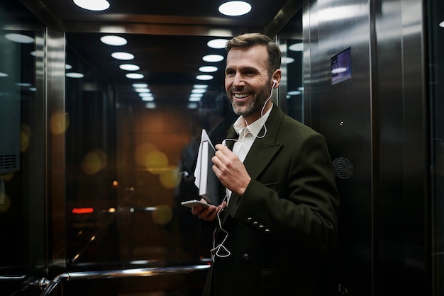Retrato del empresario sonriente escuchando música en el ascensor
