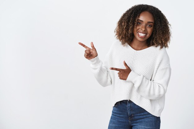 Retrato encantador despreocupado sonriente mujer afroamericana de pelo rizado apuntando hacia la izquierda