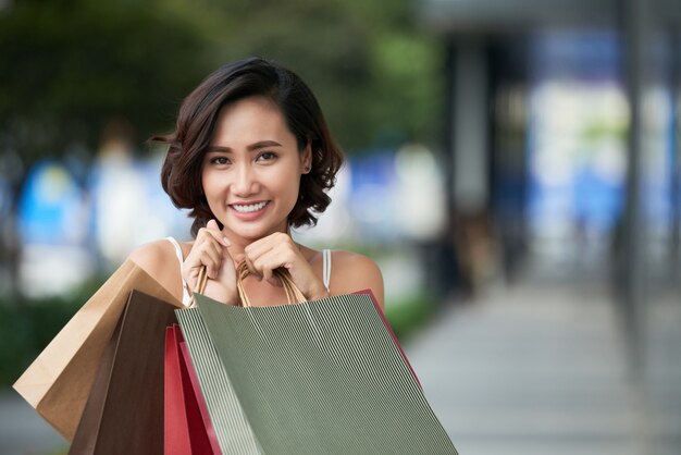 Retrato de encantadora chica compradora compulsiva de pie con una pila de bolsos de compras al aire libre