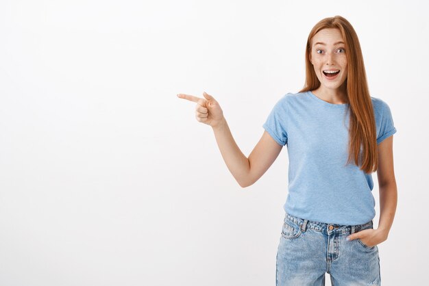 Retrato de encantadora chica pelirroja guapa entretenida complacida y feliz con pecas jadeando con una sonrisa feliz impresionado divirtiéndose apuntando a la izquierda