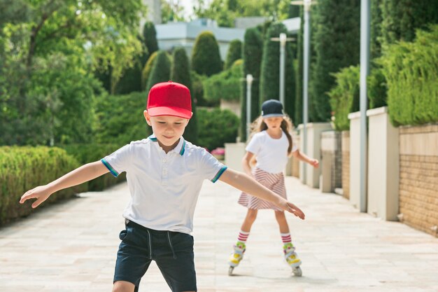 Retrato de una encantadora pareja de adolescentes patinando juntos sobre patines en el parque. Adolescente, caucásico, niño y niña