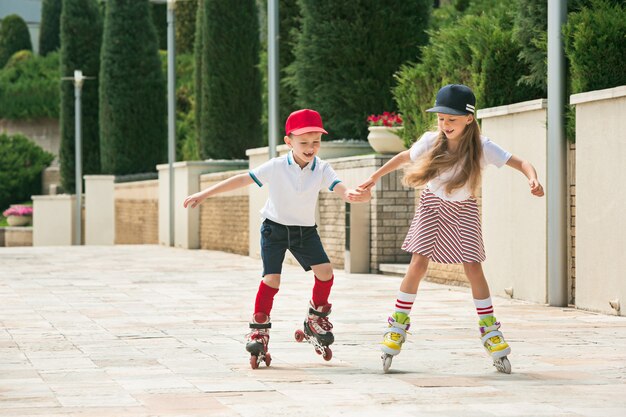 Retrato de una encantadora pareja de adolescentes patinando juntos sobre patines en el parque. Muchacho y muchacha caucásicos adolescentes. Ropa colorida para niños, estilo de vida, conceptos de colores de moda.