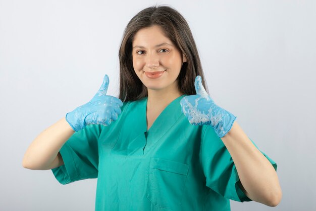 Retrato de una enfermera o un médico sonriente en uniforme verde que muestra los pulgares para arriba.