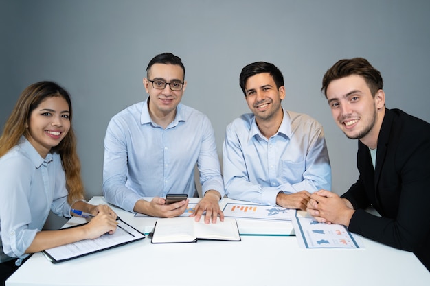 Retrato de equipo de negocios feliz sentado a la mesa y sonriendo