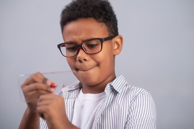 Retrato de un escolar concentrado serio en espectáculos escribiendo con un lápiz en la diapositiva