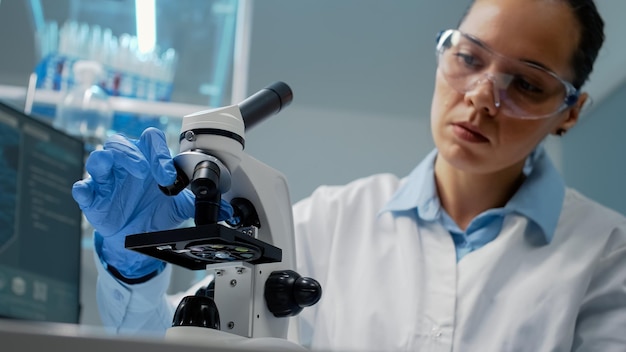 Retrato de especialista mediante microscopio científico en laboratorio con lente con lupa para prueba de ADN y bacterias. Doctor con guantes estudiando muestra con equipo biológico