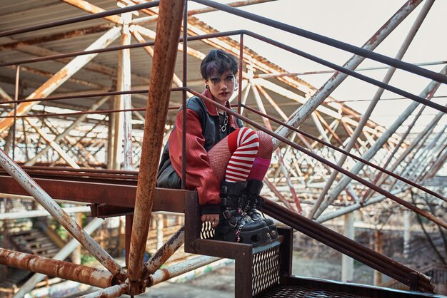 Retrato estético pop punk de mujer posando sobre estructura metálica en escaleras