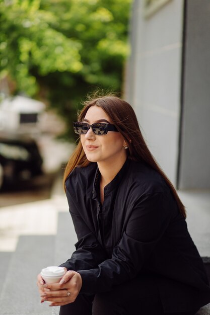 Retrato de estilo de vida al aire libre de la impresionante chica morena. Tomando café y caminando por las calles de la ciudad.