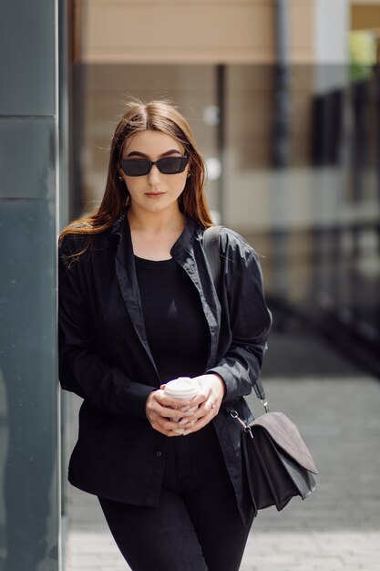 Retrato de estilo de vida al aire libre de la impresionante chica morena. Tomando café y caminando por las calles de la ciudad.