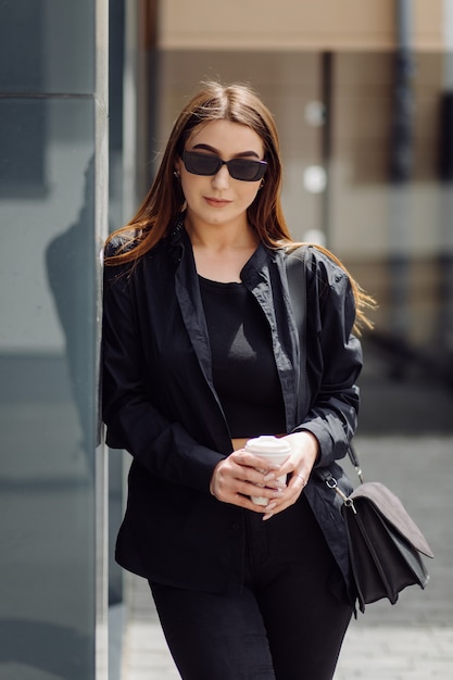 Retrato de estilo de vida al aire libre de la impresionante chica morena. Tomando café y caminando por las calles de la ciudad.