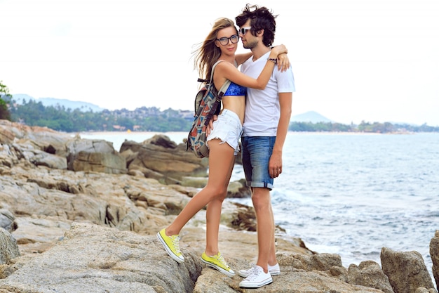 Retrato de estilo de vida al aire libre de la joven hermosa pareja de enamorados posando y divirtiéndose en la bonita playa de piedra, colores suaves.