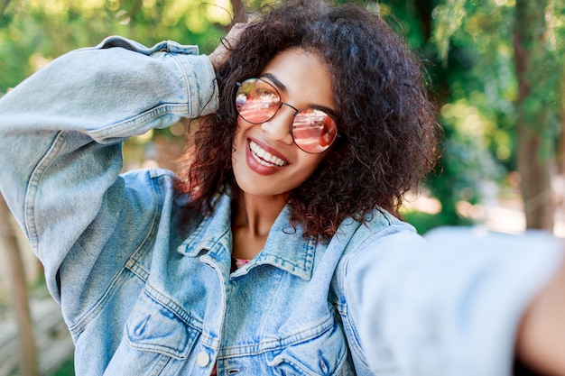 Retrato de estilo de vida al aire libre de sonriente mujer negra con gafas rosas