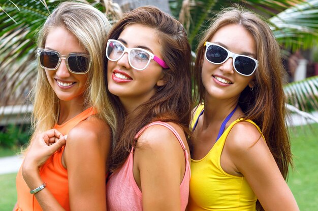 Retrato de estilo de vida brillante moda al aire libre de tres jóvenes mujeres bonitas con vestidos de verano brillantes y gafas de sol de cerca. final sonriente disfrutar de las vacaciones.