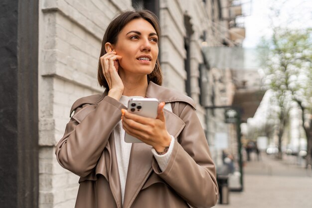 Retrato de estilo de vida callejero de mujer morena de negocios europeos con estilo en abrigo de cuero posando al aire libre