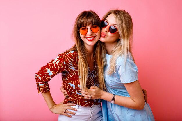 Retrato de estilo de vida de felices dos mejores amigas hermanas hermanas, posando y divirtiéndose juntos en la pared rosa