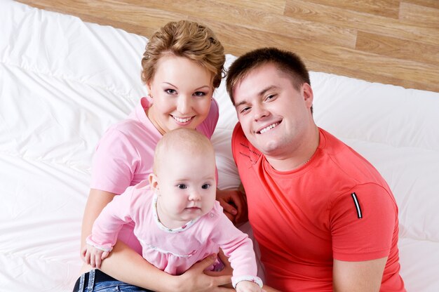 Retrato de estilo de vida de la hermosa joven familia feliz acostado en la cama en casa - ángulo alto