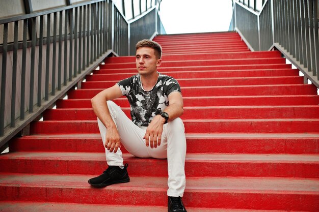 Retrato de estilo de vida de un hombre guapo posando en las escaleras rojas del tonnel de la ciudad