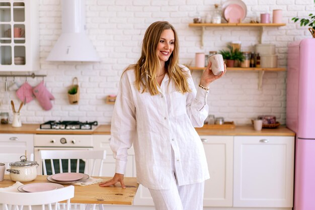 Retrato de estilo de vida interior mujer vestida con traje de lino blanco preparar comida en su cocina, ama de casa perfecta, disfrutar de su tiempo en casa.