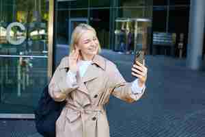 Foto gratuita retrato de estilo de vida de una joven moderna linda chica video chateando en la calle saludándola con la mano