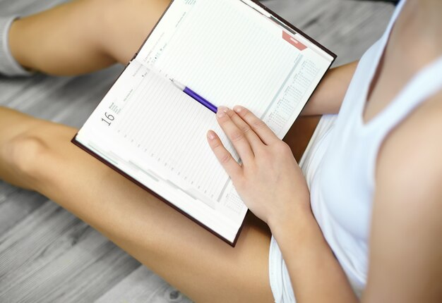 Retrato de estilo de vida de mujer joven sentada en el piso de cerca y tomando notas en su diario