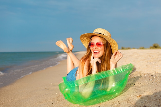 Foto gratuita retrato de estilo de vida de la mujer rubia de belleza feliz yacía en un colchón de aire tomando el sol en la playa, sonriendo y disfrutando de las vacaciones de verano