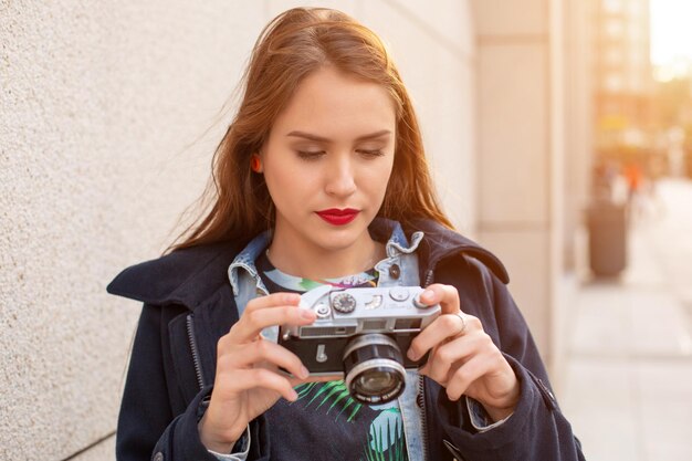 Retrato de estilo de vida sonriente de otoño al aire libre de una mujer muy joven, divirtiéndose en la ciudad con cámara, foto de viaje del fotógrafo. Hacer fotos al estilo hipster. llamarada del sol, destello solar