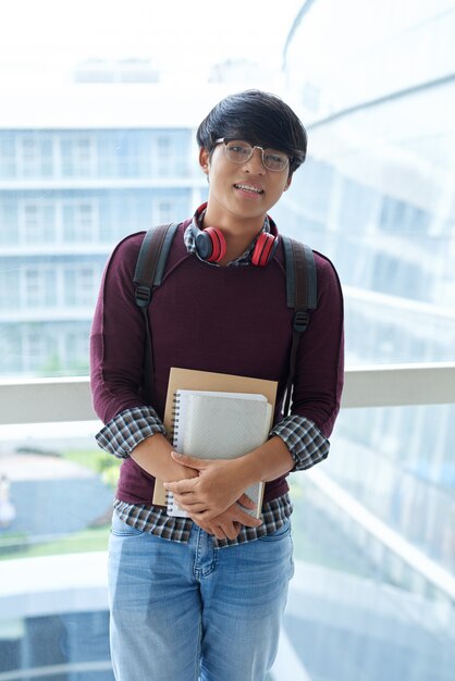 Retrato de un estudiante asiático posando con libros de estudio en el balcón de la escuela
