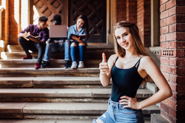 Retrato de una estudiante feliz permanecer cerca del campus con signo bien. Concepto de éxito y educación.