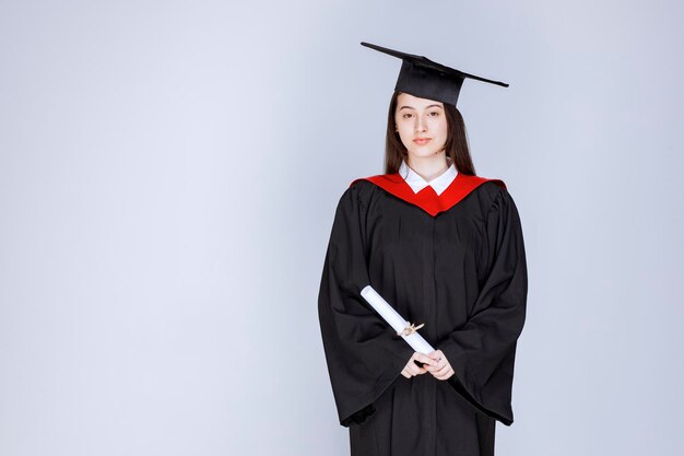 Retrato de estudiante graduado en bata con diploma y de pie. Foto de alta calidad