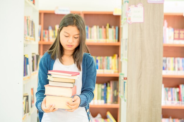 Retrato de estudiante inteligente con libro abierto que lo lee en la biblioteca de la universidad