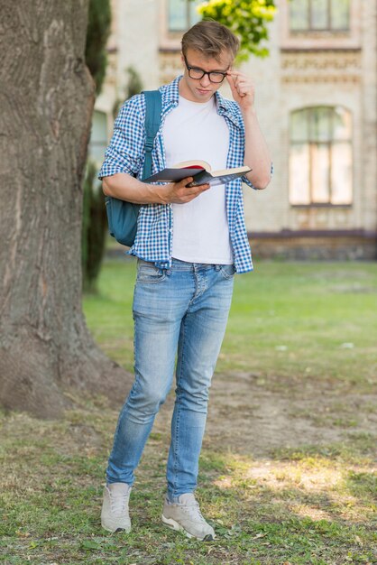 Retrato de estudiante leyendo al lado de árbol