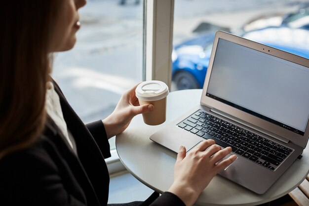 Retrato de estudiante moderno sentado en la cafetería mientras bebe café y revisa el correo con la computadora portátil