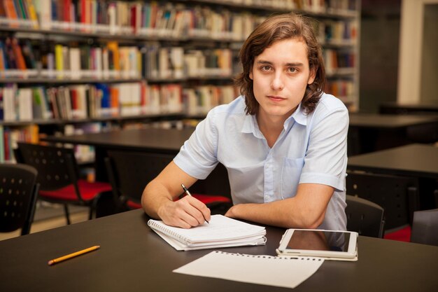Retrato de un estudiante universitario masculino tomando algunas notas y usando una tableta en la biblioteca