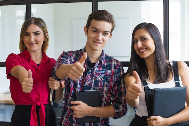 Foto gratuita retrato de estudiantes jóvenes exitosos que muestran los pulgares para arriba