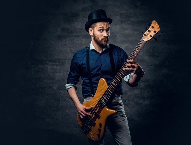 Retrato de estudio del bajista hipster vestido con sombrero cilíndrico.