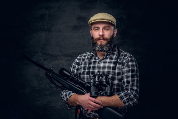 Retrato de estudio de un cazador barbudo sostiene un rifle.