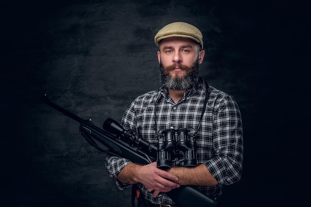 Retrato de estudio de un cazador barbudo sostiene un rifle.