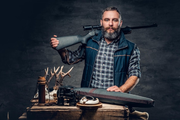 Foto gratuita retrato de estudio de un cazador moderno barbudo con su trofeo sostiene un rifle.