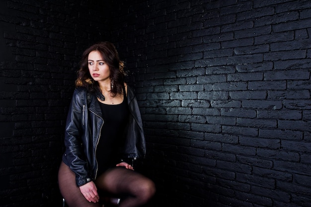 Retrato de estudio de chica morena sexy en chaqueta de cuero negro contra la pared de ladrillo