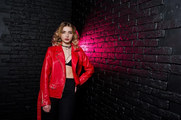 Retrato de estudio de chica rubia con chaqueta de cuero roja contra la pared de ladrillo