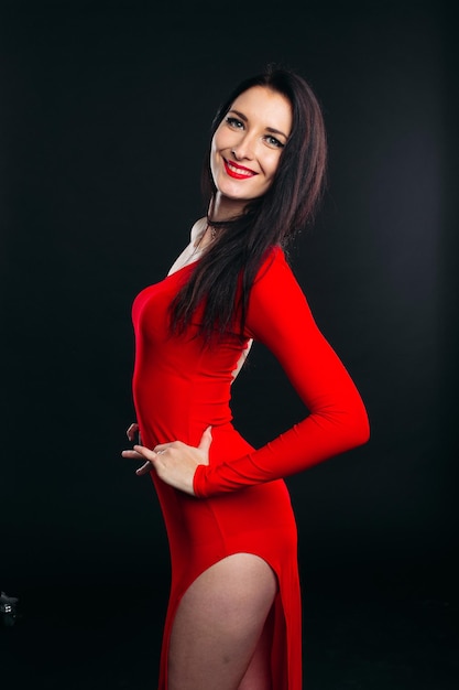 Retrato de estudio de una chica sexy y hermosa con vestido rojo glamuroso posando en un estudio gris Hermosa mujer morena antes de la fiesta de baile Mujer después del salón de belleza Copiar espacio