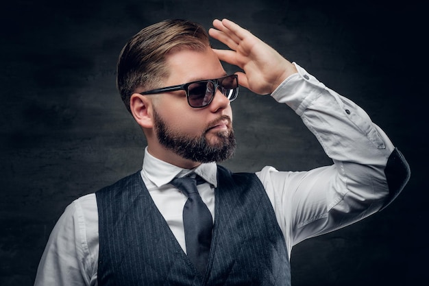 Retrato de estudio de un elegante hombre de negocios barbudo con gafas de sol con chaleco y corbata de moño.