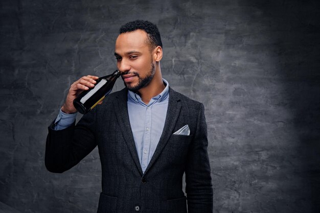 Retrato de estudio de un elegante hombre negro americano con traje que sostiene botellas de cerveza.