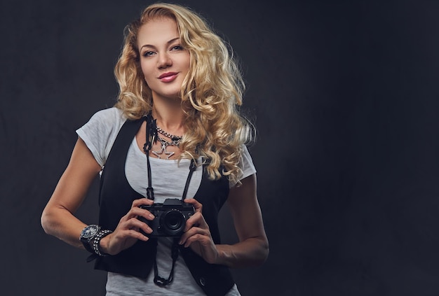 Retrato de estudio de la fotógrafa rubia tomando fotos con una cámara compacta sobre fondo gris.